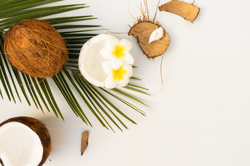 Summer flat lay scene with palm leaves and frangipani flowers with coconut fruits on wooden background with copy space