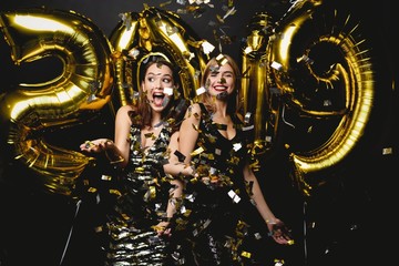Beautiful Women Celebrating New Year. Happy Gorgeous Girls In Stylish Sexy Party Dresses Holding Gold 2019 Balloons, Having Fun At New Year's Eve Party. Holiday Celebration. High Quality Image