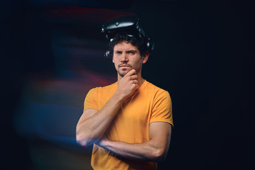 Portrait of a pensive male with bristle in yellow shirt wearing virtual reality goggles.