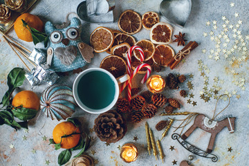 Fototapeta na wymiar New Year or Christmas composition with blue tea, tangerines, dry oranges, cones, cinnamon, gifts,candles, candies and toys on light rustic table. Seasonal home decoration, holiday food, top view