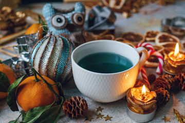 New Year or Christmas composition with blue tea, tangerines, dry oranges, cones, cinnamon, gifts,candles, candies and toys on light rustic table. Seasonal home decoration, selective focus