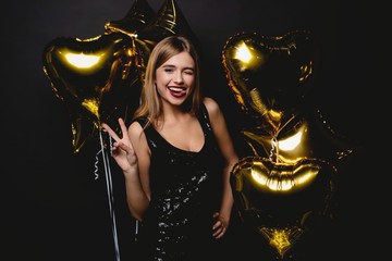 Cheerful woman with balloons laughing on black background.