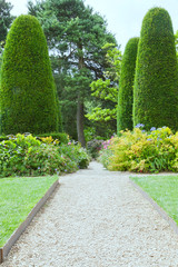 Gravel walking path in flowering summer garden between flowers, shrubs and trees . - 232869176