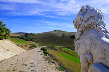 Long road in the green fields and sculpture of lion