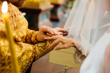 View of priest put on ring on hand of brides hand, pose in Christian church during wedding...