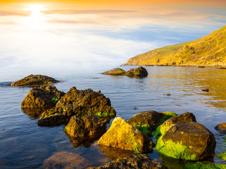 Obrazy  spokojna zatoka morska z kamieniem w wodzie o zachodzie słońca