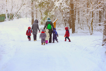Group of unrecognizable litle kids with teachers of kindergarten, back to us, walk holding hands in snowy park, winter leisure, active lifestyles