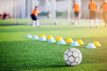 Football on green artificial turf with blurry of maker cones and football players are training.