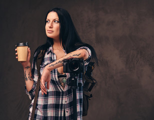 Tattooed girl holding a takeaway coffee while leaning on a camera in a studio.