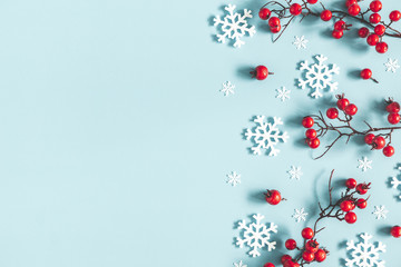 Christmas or winter composition. Frame made of snowflakes and red berries on pastel blue...