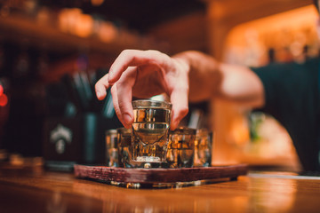 Bartender is pouring tequila into glass against the background of the bar. - obrazy, fototapety, plakaty