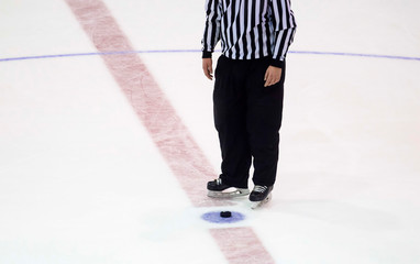 black hockey puck and referee legs on ice rink. Winter sport.
