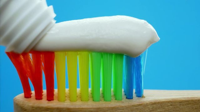 Toothpaste squeezed from tube into rainbow wooden brush for tooth cleaning isolated on blue background