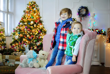 Дети ждут чудо в Новый год. С новым годом! Счастливого Рождества! Новогодняя елка с рождественскими игрушками. Брат с сестрой на диване.
