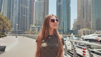 A young girl with long hair and a good mood walks along the embankment of Dubai Marina.