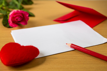 red envelope with shape heart pillow on text love and rose, sheet of paper and on wooden background