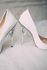 A pair of white wedding shoes with rings on a stool