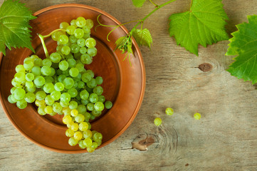 Ripe grape cluster of white grapes in a bowl on a wooden table with green leaves of grapes. Vintage...