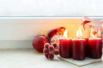 Christmas styled scene with four red burning candles on windowsill with frozen window and copy space