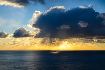 Beautiful sunset glowing orange and yellow across the horizon under dramatic clouds and dark bue sky over the Pacific Ocean along California's Big Sur coast