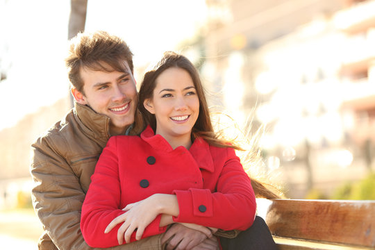 Happy couple looking away in winter on a bench