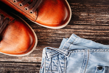 Brown leather men's boots and blue jeans on a dark wooden background