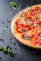 Half of italian pizza and fresh basil leaves on a dark backgroud, close up. Traditional italian cuisine