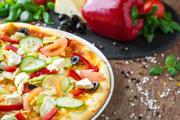 Vegetarian pizza with vegetables and ingredients on a wooden background, close up. Healthy food