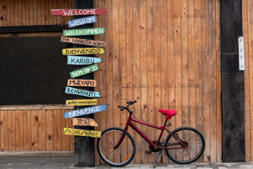 Red Bike Next to a Post with Welcome Signs in Several Different Languages.  English, Afrikaans,...