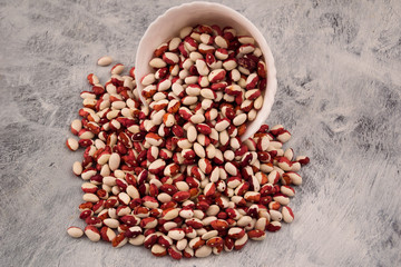 Beans unusual color brown and white, scattered from a white bowl on a wooden background.