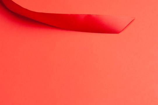 The slanted tip of a medium-width red shiny satin ribbon splayed on the top portion of a softly graduated red paper background in horizontal image format.