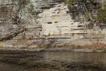 Stream flowing by a rock wall, winter, horizontal aspect