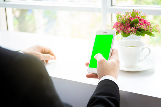 Business man in black suit using a smartphone in the coffee bar close up.  Smartphone isolated the screen with the green screen for editing.