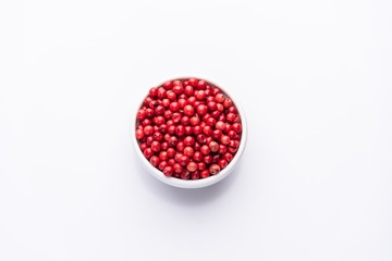 White bowl of Pink Pepper, Brazil Pepper, Rose pepper, Schinus terebinthifolius seeds over white background, top view