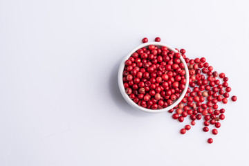 White bowl of Pink Pepper, Brazil Pepper, Rose pepper, Schinus terebinthifolius seeds over white background, top view