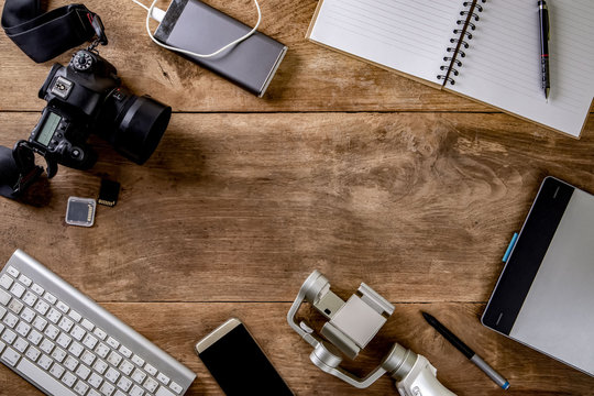 Top view vintage style of photographer consisting on a cameras, a keyboard, a smart phone, notebook on a wooden desk background