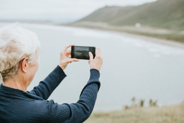 Elderly woman capturing a photo of the ocean