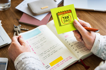 Hand holding a sticky note pad with tax day on it