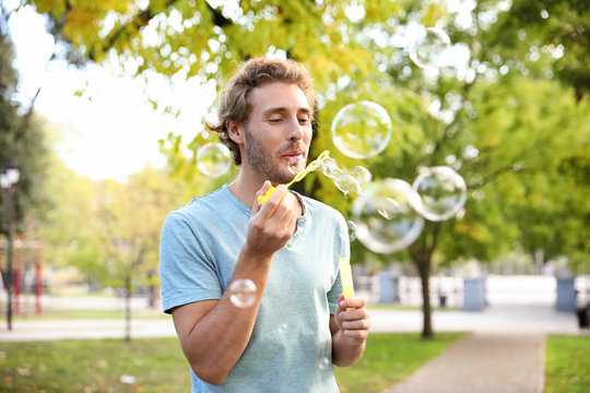 Young man blowing soap bubbles in park