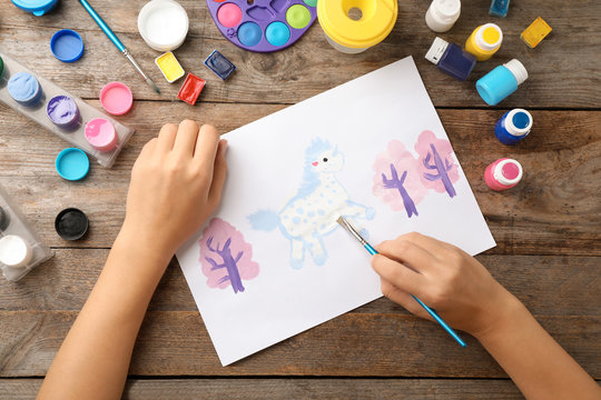 Girl painting picture of unicorn on table, top view