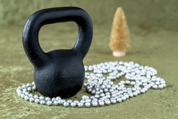 Naklejka na ściany i meble Black kettlebell on a green velvet background with silver bead garland, holiday fitness, gold tree in background