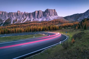 Foto op Canvas Wazig autokoplampen op kronkelende weg in de bergen bij zonsondergang in de herfst. Spectaculair landschap met asfaltweg, lichte paden, bos, rotsen en paarse lucht & 39 s nachts in de herfst. Auto rijden op rijbaan © den-belitsky