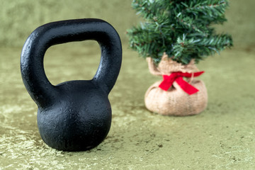 Naklejka na ściany i meble Black kettlebell on a green velvet background, holiday fitness, Christmas tree in background