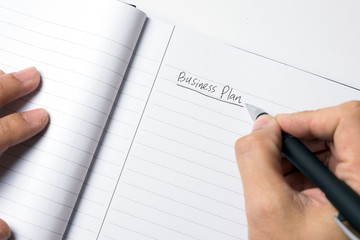 Close-up of male hand writing down business plan strategy in notebook with pen