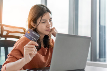 Young asian woman holding credit card and use laptop for purchase product on internet in home office, Cyber Monday shopping online concept, Copy space.