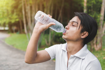 Exercise and healthy concept, Young asian man runner relaxing drinking water in bottle in the park outdoors after sport at early morning time.