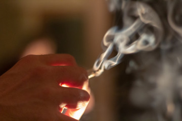 A hand holding a marijuana cigarette or joint with a large plume of thick smoke coming from it.