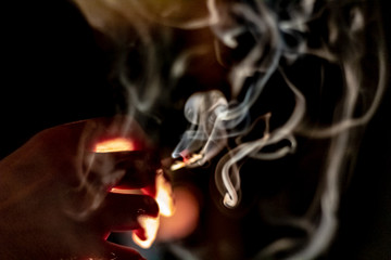 A hand holding a marijuana cigarette or joint in between two fingers as smoke swirls around.