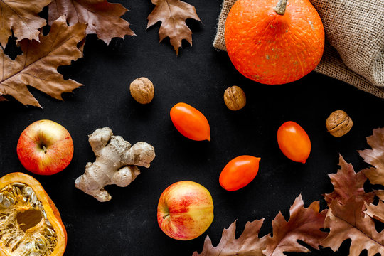 Autumn garden harvest. Dried leaves, pumpkin, apple, tomatoes, ginger and nuts on black background top view