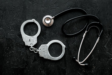 Medical lawsuit. Arrest for medical crime concept. Handcuff near stethoscope on black background top view